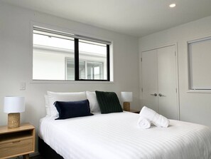 Un letto rifatto con lenzuola bianche, due lampade ai lati e una finestra sopra il letto.