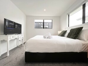 Een moderne slaapkamer met een groot bed, een flatscreen televisie, een raam en een wit bureau.