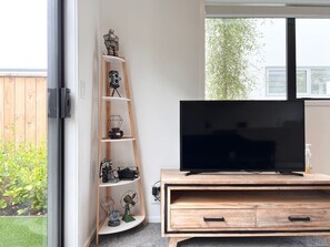 A modern living room with a wooden entertainment unit, a flat-screen TV, and a decorative ladder shelf with various items.