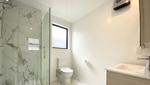 Un baño con cabina de ducha de vidrio, inodoro y lavamanos con gabinete de madera.