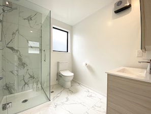 A bathroom with a glass shower enclosure, a toilet, and a sink with a wooden cabinet.