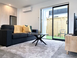 A modern living room with a dark sofa, a round coffee table, and a sliding glass door leading to a backyard.
