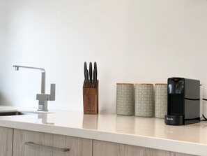 Un piano di lavoro in cucina con un rubinetto moderno, un portauova in legno, tre contenitori decorati e una macchina da caffè Breville.