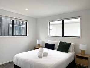 A hotel room with a large bed, two bedside tables, a window, and a lamp on each table.