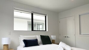 Una cama bien tendida con sábanas blancas, dos lámparas de noche y una ventana sobre la cama.