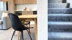 A modern kitchen with wooden cabinets, a dining table with chairs, and a staircase with grey carpeted steps.