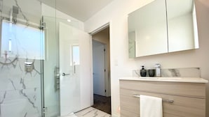 Ein modernes Badezimmer mit einer Duschkabine aus Glas, einem Marmorboden, einem Holzwaschtisch mit Spiegel und einem Handtuch an der Tür.