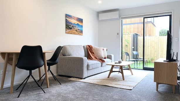 Ein modernes Wohnzimmer mit grauem Sofa, schwarzen Sesseln, einem Holztisch und einem Fernsehschrank.