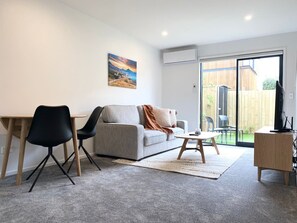 Ein modernes Wohnzimmer mit grauem Sofa, schwarzen Sesseln, einem Holztisch und einem Fernsehschrank.
