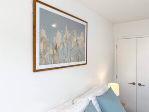Ein Schlafzimmer mit Bett, Kissen, einem Nachttisch, einem gerahmten Bild und einer Tür.