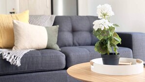 Un salon moderne avec un canapé gris, une table basse ronde en bois et une plante en pot ornée de fleurs blanches.