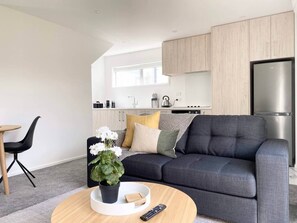 A modern living room with a grey sofa, a round coffee table, and a kitchen in the background. - Salisbury courtyard retreat with a workspace in Christchurch (Christchurch)