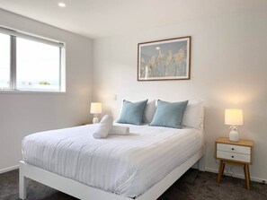 A neatly made bed with white bedding and two pillows, a small bedside table with a lamp, and a framed picture on the wall. - Salisbury courtyard retreat with a workspace in Christchurch (Christchurch)