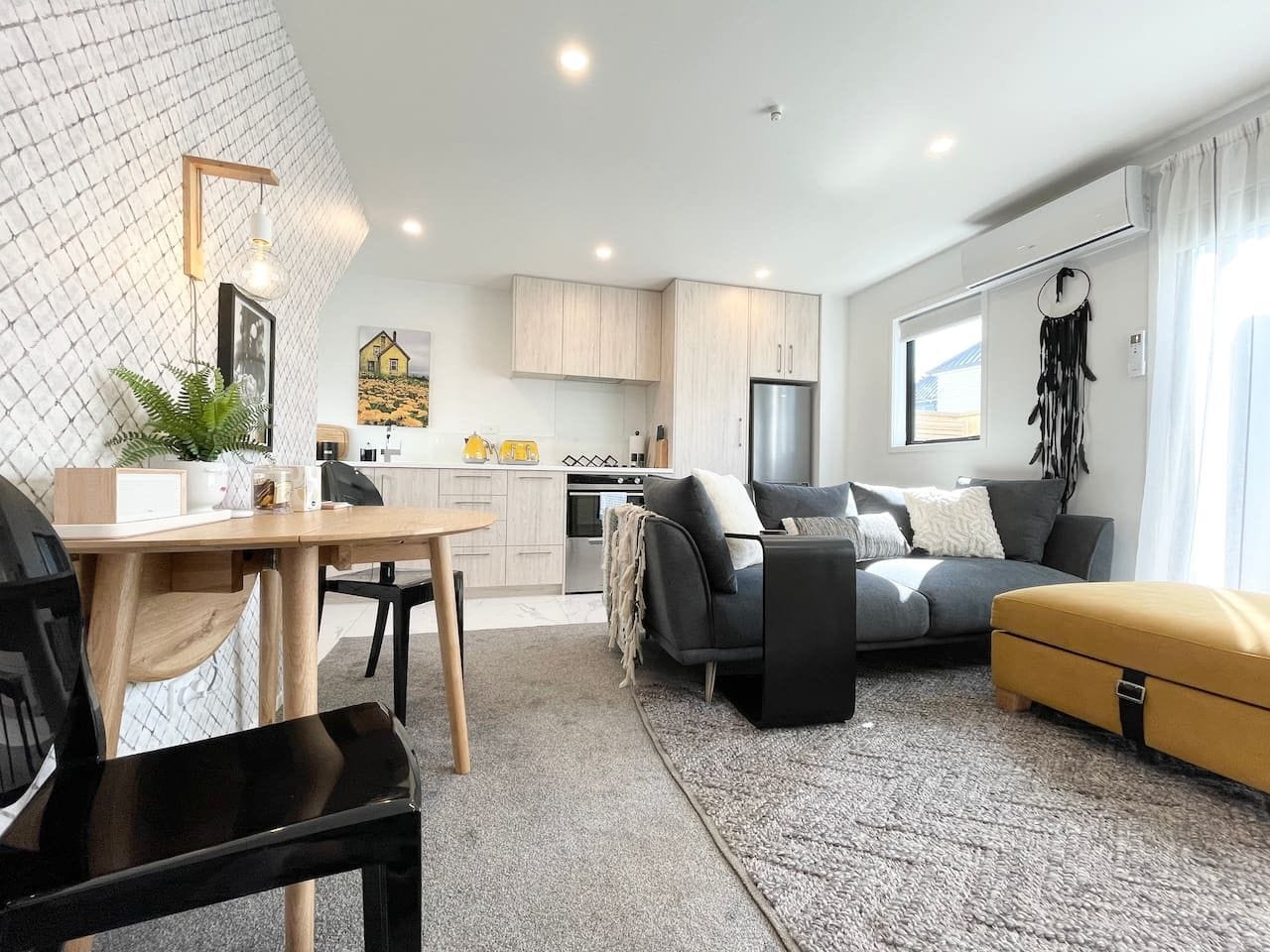 Un salon moderne comprenant un canapé, un pouf et un coin repas avec une table et des chaises.