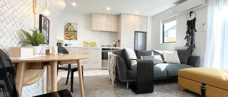 En moderne stue med sofa, skammel og et spiseområde med bord og stole.