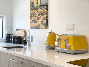 A modern kitchen with a white countertop, two yellow appliances, a coffee maker, and a painting on the wall. - Bambina design retreat opposite Hagley Park in Christchurch (Christchurch)