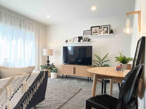 A modern living room with a flat-screen TV, a dining table, and a sofa. - Bambina design retreat opposite Hagley Park in Christchurch (Christchurch)