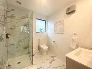 A modern bathroom with a glass shower enclosure, a toilet, a sink, and a window with a plant. - Bambina design retreat opposite Hagley Park in Christchurch (Christchurch)