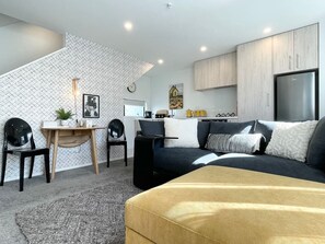 A modern living room with a sofa, a coffee table, and a dining area with chairs and a small table. - Bambina design retreat opposite Hagley Park in Christchurch (Christchurch)
