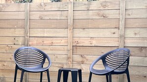 Two black plastic chairs with slatted backs and a small black table in front of a wooden fence.
