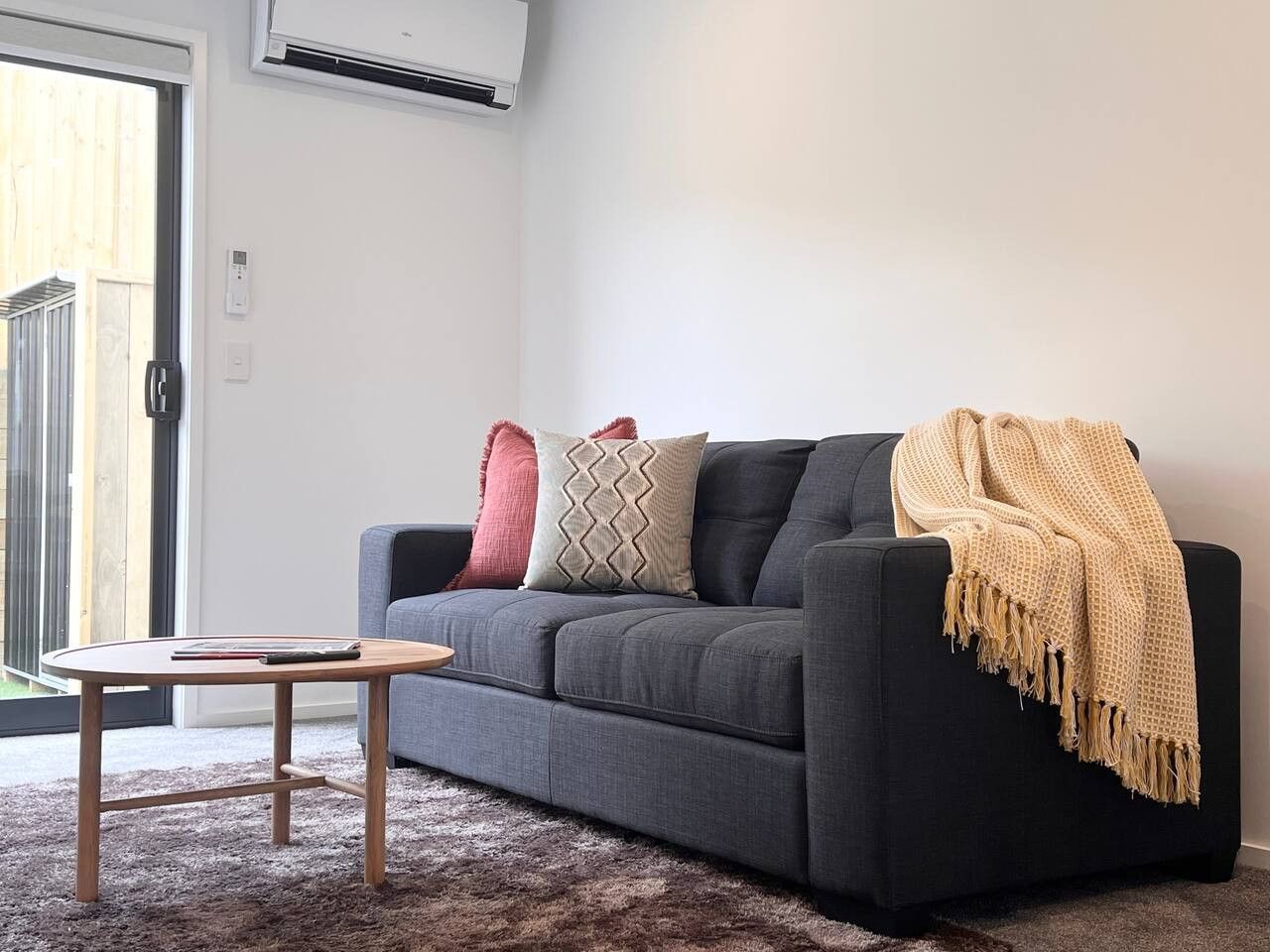 Uma sala de estar moderna com um sofá cinzento, uma mesa de centro de madeira e um cobertor bege.