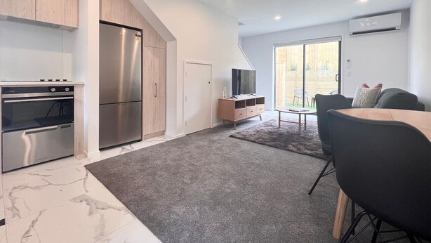 A modern kitchen with stainless steel appliances, a dining area with a table and chairs, and a sliding glass door leading to a balcony.