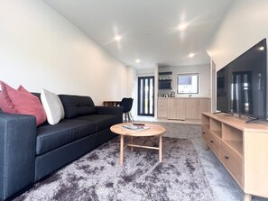 Ein modernes Wohnzimmer mit einem dunklen Sofa, einem runden Couchtisch und einem Fernseher auf einem Holzboden.
