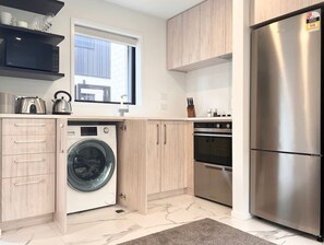 Eine kompakte Küche mit Einbauwaschmaschine, Backofen und Kühlschrank, ausgestattet mit hellen Holzschränken und einem großen Fenster.