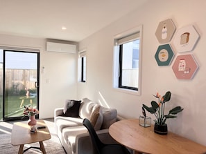 A modern living room with a sofa, a coffee table, and a dining table. There are hexagonal wall art pieces and a potted plant on the dining table.