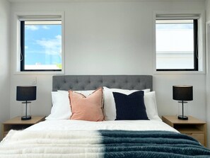 A bedroom with a grey tufted headboard, a white and blue striped blanket, and two bedside tables with lamps. - Salisbury courtyard stay with a 65-inch TV in Christchurch (Christchurch)