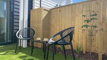 An outdoor patio with two chairs and a table, a wooden fence, and a small plant.