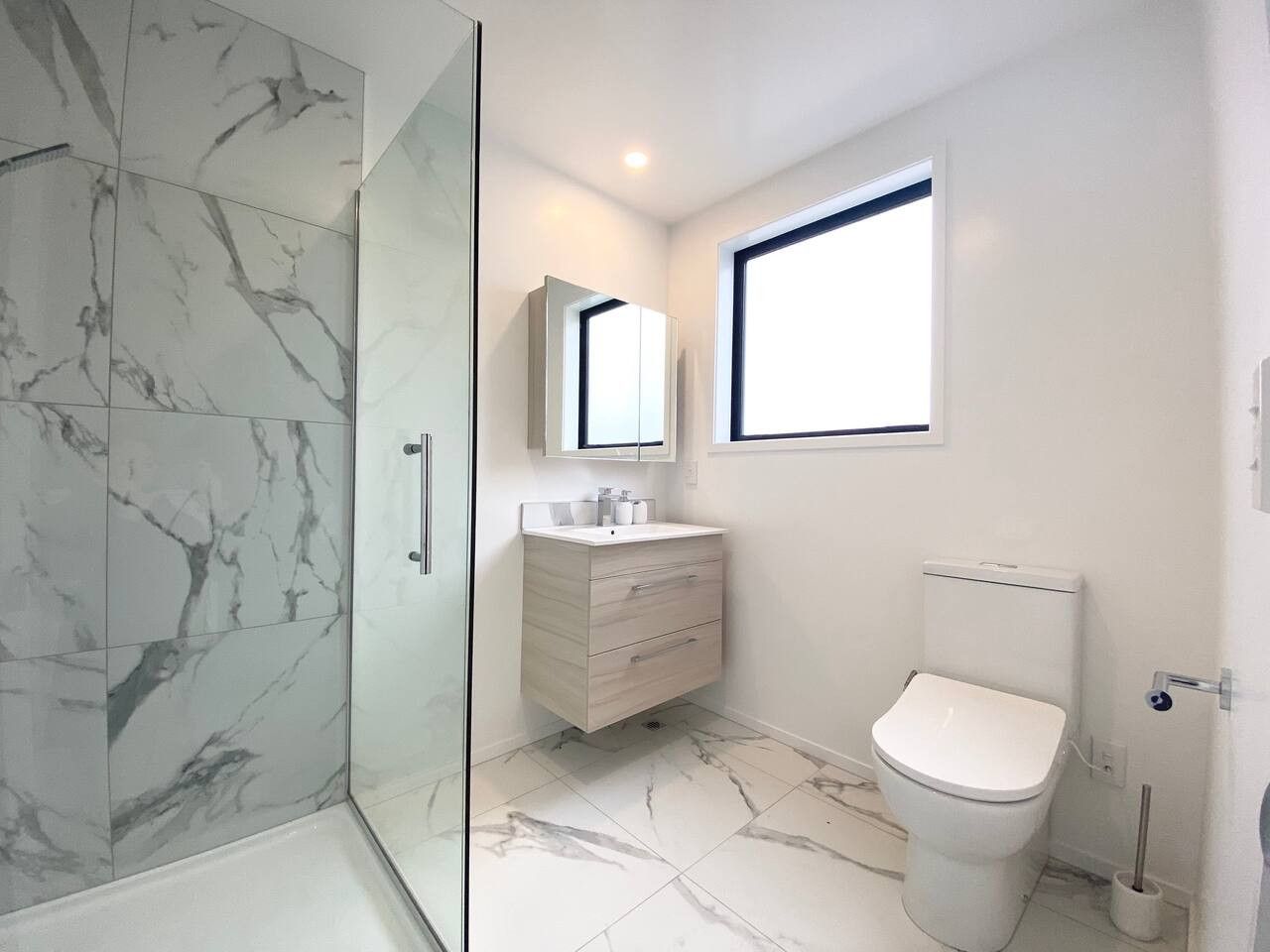 A modern bathroom with a glass shower enclosure, a white vanity with a mirror, and a toilet.