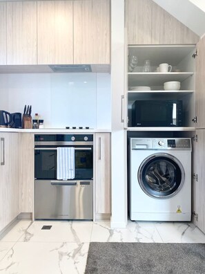 Una cucina moderna con forno integrato, microonde e lavatrice, più un piccolo ripiano con tazze e piatti.