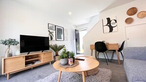 Uma sala de estar moderna com televisão de tela plana, painel de entretenimento de madeira, mesa de centro redonda e um sofá cinza.