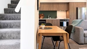 Um espaço de estar moderno com escada, área de jantar com mesa e cadeiras de madeira, cozinha com armários de madeira e um sofá cinzento.