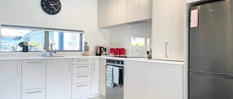 Een moderne keuken met lichte houten keukenkastjes, een roestvrijstalen koelkast en een inbouwoven.