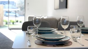Una mesa de comedor dispuesta con platos, vasos y cubiertos en una habitación moderna con vistas a través de un ventanal.