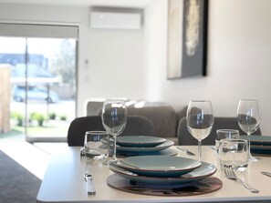 A dining table set with plates, glasses, and cutlery in a modern room with a view through a glass door.