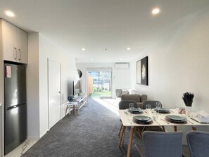 Una cocina moderna con refrigerador empotrado, un comedor con una mesa dispuesta para cuatro personas y un sofá al fondo.
