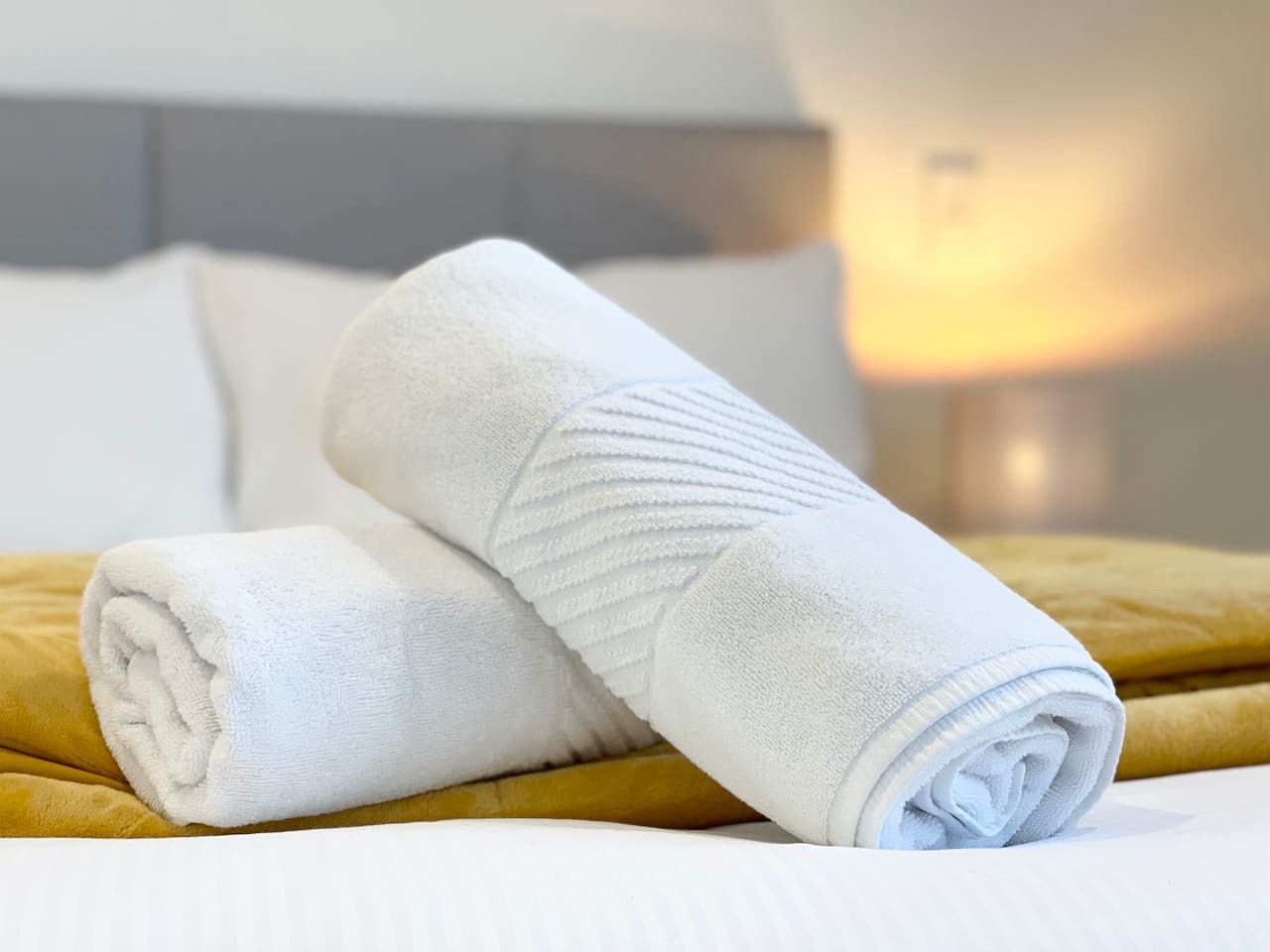 A neatly made bed with two rolled white towels and a mustard-colored blanket.
