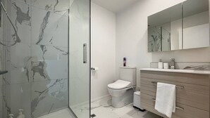 Un baño moderno con cabina de ducha de vidrio, inodoro, tocador con espejo y suelo de mármol.