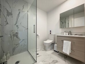 A modern bathroom with a glass shower enclosure, a toilet, a vanity with a mirror, and marble flooring.