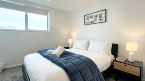 Una habitación de hotel moderna con una cama grande, una mesita de noche con lámpara y una fotografía enmarcada en la pared.