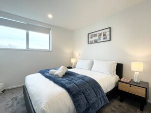 A modern hotel room with a large bed, a bedside table with a lamp, and a framed photo on the wall.