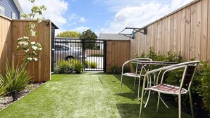 Un patio con césped artificial, valla de madera y dos sillas de metal.