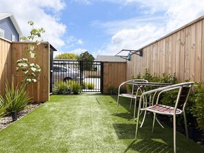 A backyard with artificial grass, a wooden fence, and two metal chairs.