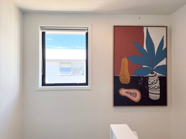A room with a window, a painting, and a white shelf.