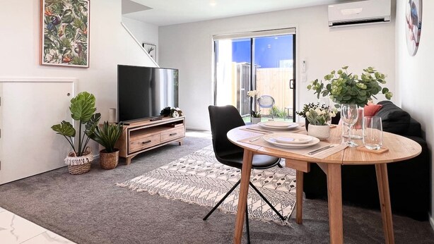 Een moderne woonkamer met een eettafel, een flatscreen televisie en een trap die leidt naar een balkon.