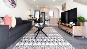 Een moderne woonkamer met een zwarte bank, een ronde salontafel en een flatscreen televisie op een houten dressoir.