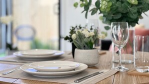 Een eettafel gedekt met borden, bestek en een vaas met bloemen.